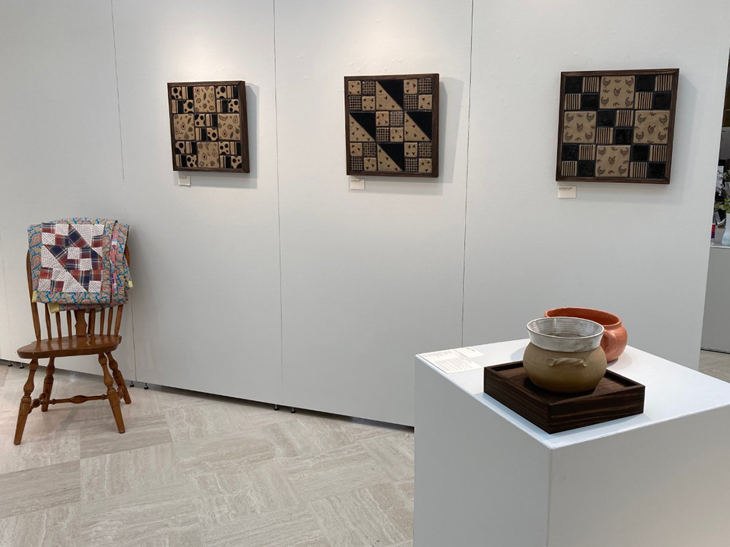 three tile quils on wall with reference quilt over chair and cooking vessel in foreground
